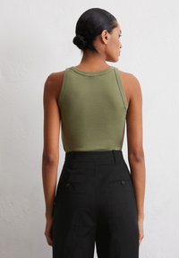 Top sans manches vert olive avec un col arrondi, associé à un pantalon taille haute noir avec deux poches arrière et une texture lisse.