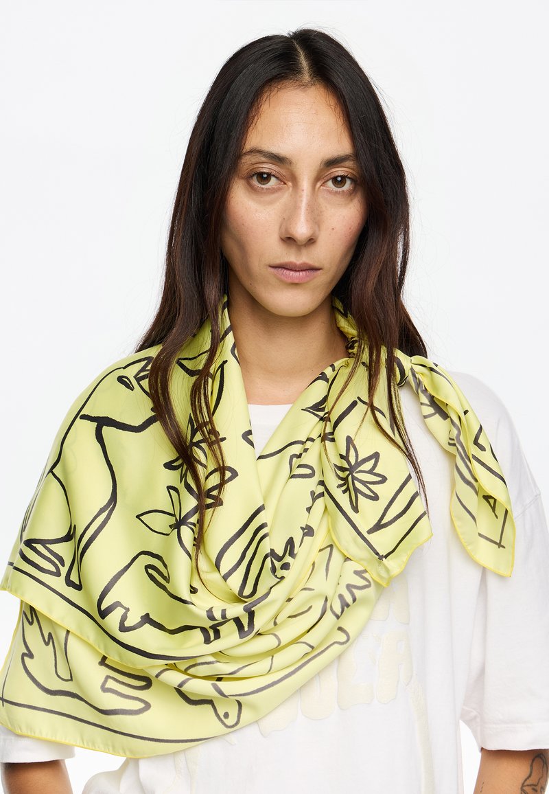 Bufanda de seda en amarillo claro con dibujos en líneas de animales y flores en negro. Textura suave, diseño fluido y detalles de dobladillo fino.