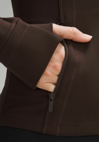 Brown performance jacket featuring a zippered pocket, smooth texture, and flatlock seams on the cuffs and body for added durability.