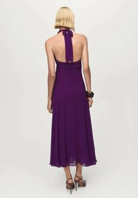 Lila Halfter-Back-Kleid mit einem fließenden Rock, der eine Bindung am Hals und ein offenes Rückendesign aufweist. Glattes Material mit einer leichten Textur.