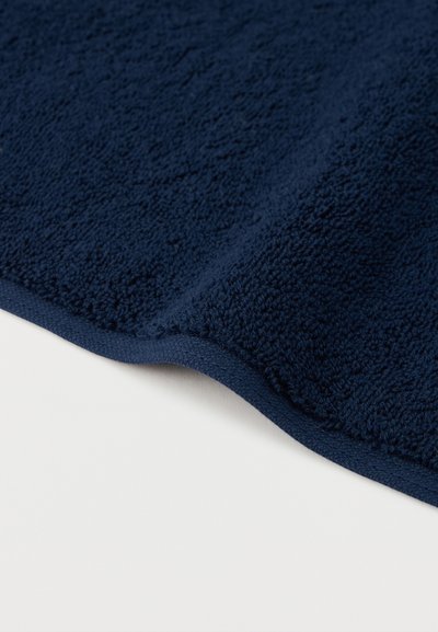Dark blue terry cloth fabric with folded edge on a white surface, showing texture and stitching detail.