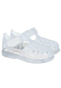 Sandalias blancas translúcidas con diseño recortado y correas ajustables. Fabricadas con un material flexible y una suela plana y contorneada para mayor comodidad.