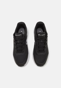 Svarta träningsskor har en ovandel i mesh, snörningssystem och en vit gummisula med texturerade detaljer. Logotypen visas på tungan.