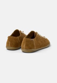 Zapatillas de gamuza marrón con cordones blancos, puntera redondeada y suela de goma flexible. Presentan una costura bordada y una pequeña etiqueta de marca en la parte trasera.