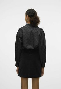 Svart satengbluse med et subtilt preget mønster og puff-sleeves, sammen med et svart kordfløyels mini-skjørt med en bakre glidelås.