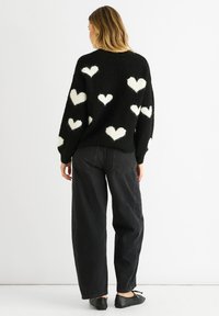 Black knitted sweater with white heart patterns, round neckline, and oversized fit. Paired with black baggy jeans and flat shoes.