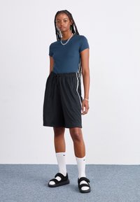 Mørkeblå kortermet t-skjorte kombinert med svarte mesh-shorts med snor i livet og sidelister. Brukt med svarte sandaler og hvite sokker.