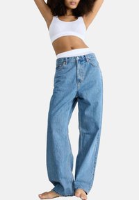 Hoge taille lichtblauwe denim jeans, relaxte pasvorm, met zichtbare stiksels en voorzakken. Gepaard met een witte cropped tanktop.