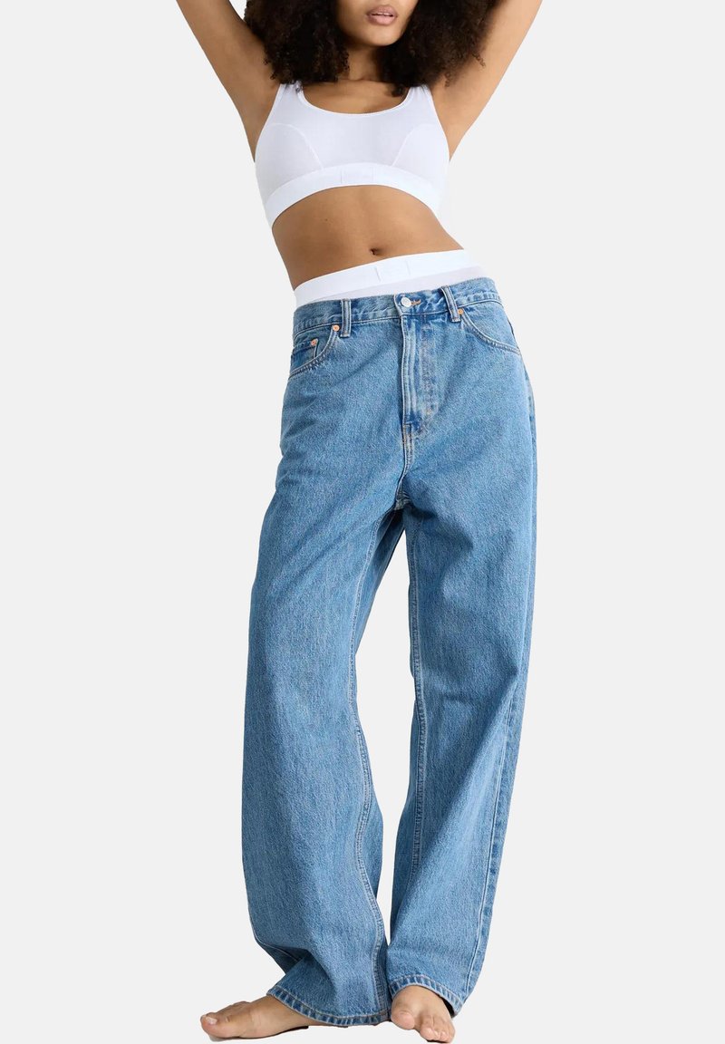 Hoge taille lichtblauwe denim jeans, relaxte pasvorm, met zichtbare stiksels en voorzakken. Gepaard met een witte cropped tanktop.