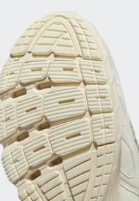 Ljusgrå gummisula med texturerade greppmönster, inklusive hexagonala och linjära designer, samt synliga varumärkesdetaljer.