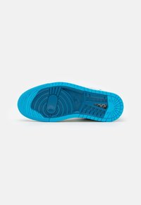 Semelle de chaussure de sport bleu vif avec des motifs circulaires et une adhérence texturée, vue de dessous sur fond blanc uni.