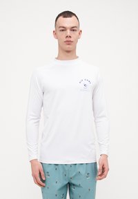 Langermet hvit rash guard med blå "Rip Curl" logo og bølgediagram, laget av lett materiale, egnet for vannsport.