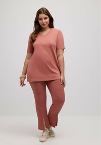 Lichtroze loungewear set met een T-shirt met korte mouwen en een V-hals, en geribbelde broek met zijsplitten, gemaakt van zachte, gestructureerde stof.