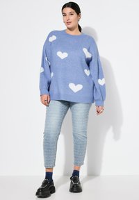 Modrý pletený svetr s bílými vzory srdcí, volný střih, kulatý výstřih, doplněný o světle modré texturované džíny a černé platformové boty.