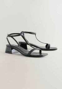 Sandalias negras con un acabado brillante, que cuentan con tiras delgadas ajustables, un diseño en T y un tacón bajo tipo bloque para estabilidad y comodidad.