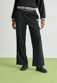 Pantaloni neri a gamba larga realizzati in un tessuto morbido, con vita elasticizzata, orlo spaccato e un piccolo logo sul davanti.