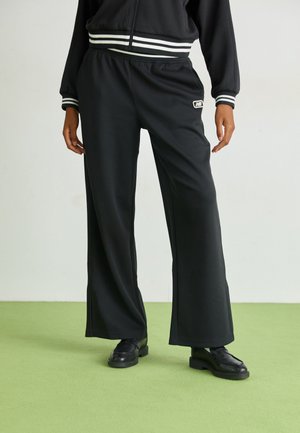 Pantaloni neri a gamba larga realizzati in un tessuto morbido, con vita elasticizzata, orlo spaccato e un piccolo logo sul davanti.