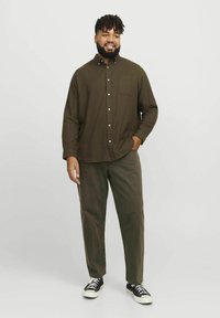 Brown button-up shirt with a chest pocket, paired with olive green pants and black sneakers. The fabric appears textured and relaxed fit.