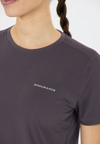 Lähikuva henkilöstä, jolla on päällään tumman violetin värinen urheilu toppi, jossa lukee rinnassa "KESTÄVYYS".