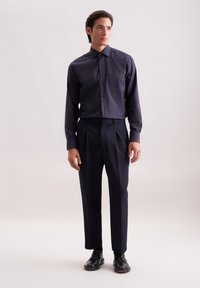 Camicia blu navy con taschino, abbinata a pantaloni scuri su misura e scarpe in pelle nera; tessuto liscio e design aderente.