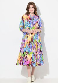 Abito a strati colorato con motivo floreale che presenta tonalità di viola, giallo e verde; chiusura frontale con bottoni e maniche a trequarti.