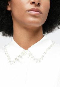 Close-up of a person wearing a white collared shirt with a pearl bead trim along the collar edges.