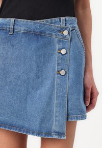 Jeanskjørt i lyseblått med omslagsdesign, med sølvfargede knapper og kontrastsøm. Glatt tekstur med en foret kant.