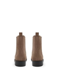 Bottines en suède marron avec des panneaux élastiques sur les côtés et des languettes de tirage. Dotées d'une semelle en caoutchouc noir lisse. Conçues avec des détails de couture verticaux.