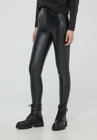 Leggings neri in ecopelle con una finitura liscia e lucida e una vita alta, abbinati a stivali alla caviglia neri con lacci e suola spessa.