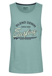 Svetle zelené tílko vyrobené z měkké tkaniny, s grafikou "Blend Denim" a "Surfing" v tmavě modré a krémové barvě.