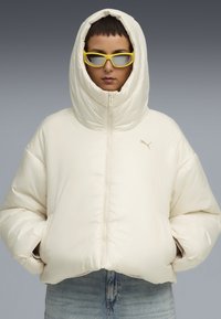 Puffjacka i off-white, med hög huva, dragkedjeslutning och ribbad mudd. Åtföljd av gula rektangulära solglasögon.