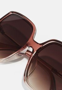 Brown-tinted oversized sunglasses with a translucent brown frame, featuring a geometric design and smooth texture on the arms.