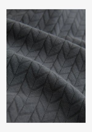 Tissu texturé en gris foncé avec un motif en chevrons, présentant une apparence tissée douce et des formes distinctes en chevron.