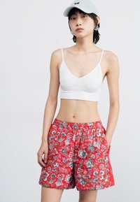Piros virágmintás rövidnadrág rugalmas derékkal és oldalsó zsebekkel, fehér crop top-pal és világoskék sapkával párosítva.