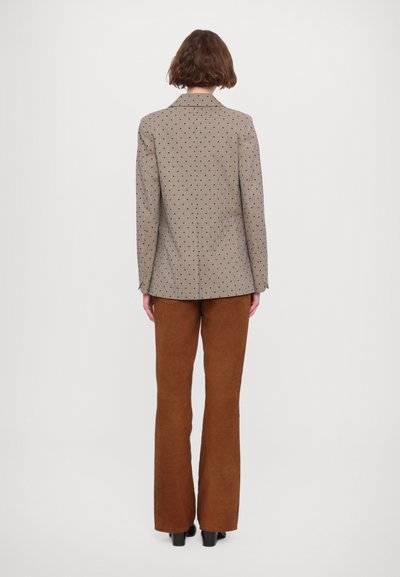 Brune fløjl flared bukser parret med en beige mønstret blazer med et rutenet design og blå accenter, set fra ryggen.