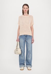 Strikket beige topp, løs passform, korte ermer; lyseblå baggy jeans med logo-broderi; kremfarget håndveske; beige joggesko.