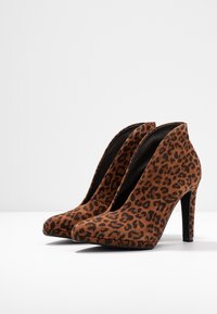 Chaussures à talons hauts en imprimé léopard marron avec une texture en suède lisse et des pointes effilées. Les talons sont fins et mesurent environ 10 cm de hauteur.