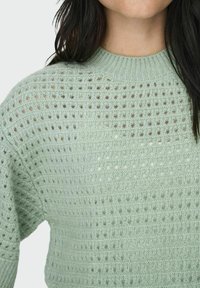Maglione lavorato a maglia verde chiaro con un motivo strutturato di punti aperti, colletto rotondo e vestibilità leggermente ampia.