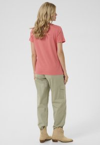 Růžové tričko s krátkým rukávem a kulatým výstřihem, kombinované s volnými světle zelenými cargo kalhotami a béžovými kotníkovými botami.