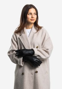 Beige wool blend coat with double-breasted design and brown buttons, paired with fitted black leather gloves. Smooth texture.
