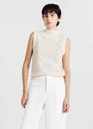 Cream sleeveless turtleneck top with diamond-patterned knit texture, paired with white high-waisted trousers featuring large pockets.