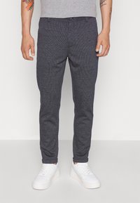 Kalhoty s námořnickým vzorem a slim fit, vyrobené z texturované látky, s knoflíkovým zapínáním. Je kombinováno s bílými teniskami.