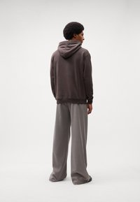 Bruine hoodie met een trekkoord en geribbelde manchetten, gecombineerd met grijze wijde broekspijpen. Zachte stoffen, neutrale kleuren, minimale details.