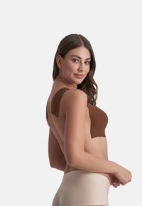 Bralette senza cuciture marrone con spalline larghe, texture liscia e design modellato. Abbinato a biancheria intima beige a vita bassa. Sfondo pulito.