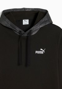 Juodas Puma džemperis su raštuota tamsiai pilka gobtuvu, juodomis raištelėmis ir baltu Puma logotipu ant krūtinės.