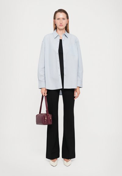 Cămașă oversized de un albastru deschis, cu nasturi, peste un top negru, asortată cu pantaloni negri evazați și o geantă mică de un burgund. Pantofi albi cu vârful ascuțit.
