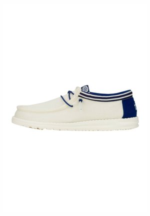 Zapato de barco de lona en crema y azul marino, con punta redonda, acentos en el talón en contraste y un cuello a rayas. Suela de goma ligera.