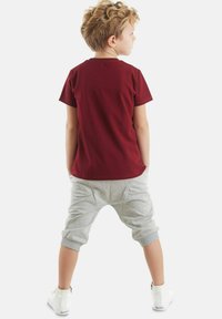 T-shirt corto maroon a maniche corte abbinato a pantaloni larghi grigio chiaro. Il tessuto appare morbido, con polsini elasticizzati e tasche laterali. Le scarpe sono bianche.