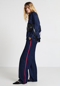 Outfit in denim con un top a maniche lunghe blu scuro e pantaloni a gamba larga con una striscia rossa laterale, abbinati a una borsa nera a tracolla.