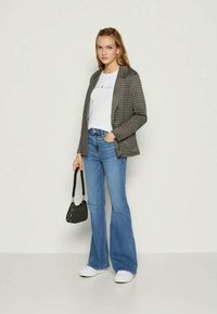 Πλαίσιο μπλέιζερ πάνω από λευκό μπλουζάκι, σε συνδυασμό με ανοιχτόχρωμα τζιν που επεκτείνονται προς τα κάτω και λευκά αθλητικά παπούτσια. Τα αξεσουάρ περιλαμβάνουν μια μικρή μαύρη τσάντα.